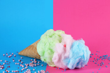 Sweet cotton candy in waffle cone on color background, closeup