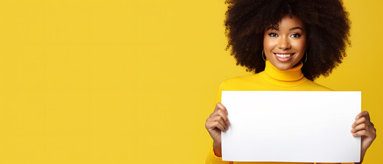 happy woman looking at a camera holding a white sign on a yellow background - copy space mockup - obrazy, fototapety, plakaty