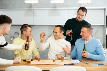 Friends drinking beer and enthusiastically playing a board game at home