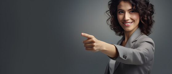 happy woman looking at a camera pointing with finger on a gray background - copy space