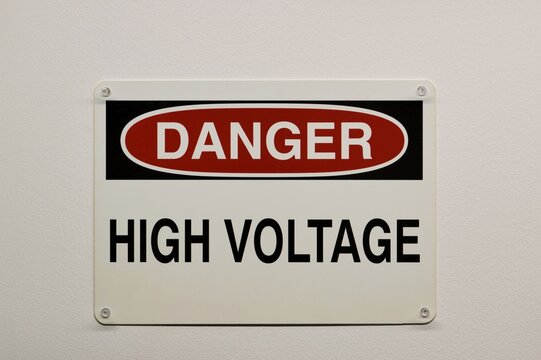 Danger High Voltage plastic warning sign isolated and attached to a white wall with push pins. Electricity safety concept.