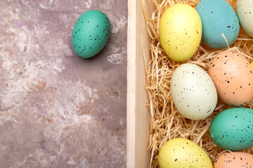 Easter, colored eggs in a wooden box on straw. View from above. Space for text