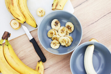 Bananas on white cutting board. Wooden table ripe banana slices isolated. Sunlight fruits. Quick...