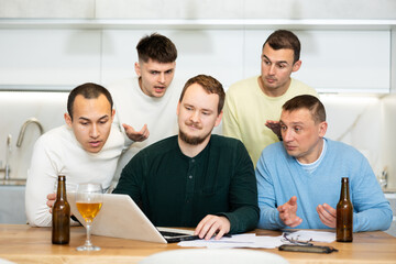 Fototapeta premium Group of male friends solving problems using laptop and drinking beer at home