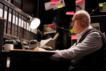 Elderly police officer working at criminal case overhours in arhive room, analyzing mysterious victim report. Senior private investigator checking crime scene evidence, confidential information