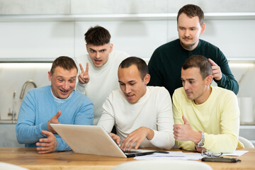 Fototapeta premium Group of interested men examining and discussing content on laptop, engaged in collaborative effort at home table
