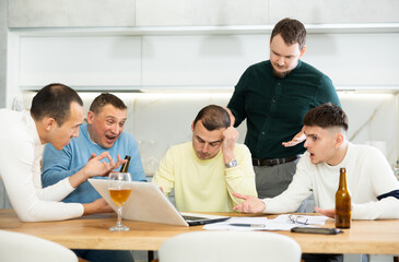 Concerned group of friends offering support to upset man receiving bad news, gathering together around laptop at home table during informal meeting with beer
