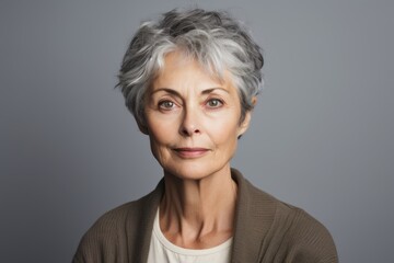 Portrait of a senior woman with grey hair against grey background.