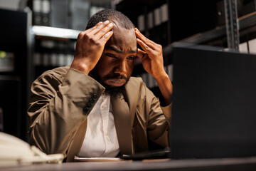 Tired cop suffering from migraine working overtime on laptop. Stressed african american police...