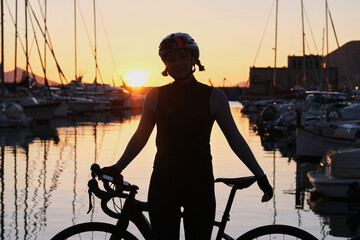 Silhouette of fit woman cyclist with her bicycle on yacht club background during a sunset. Healthy...
