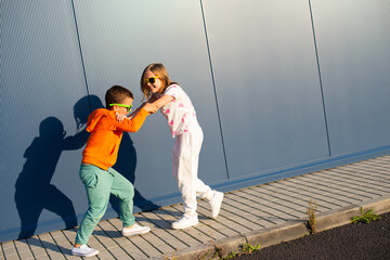 Eight-year-old boy and girl pushing each other on the street against the background of a blue wall - 729673120