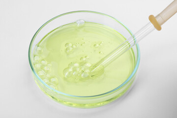 Petri dish with liquid sample and pipette on white background