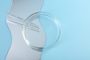 Empty petri dish, pipette and mirror on light blue background, flat lay. Space for text