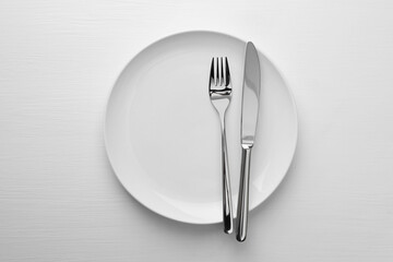 Clean plate, fork and knife on white table, top view