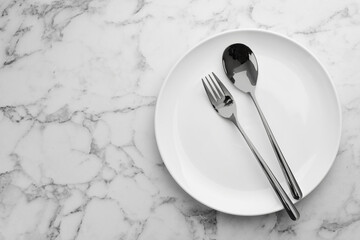 Clean plate and cutlery on white marble table, top view. Space for text
