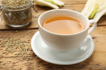 Fennel tea in cup, seeds and fresh vegetable on wooden table, closeup