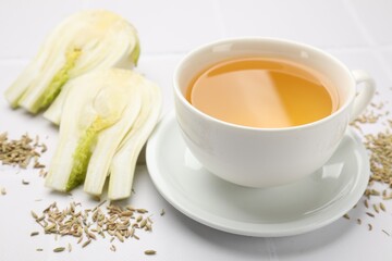 Fennel tea in cup, seeds and fresh vegetable on white tiled table, closeup