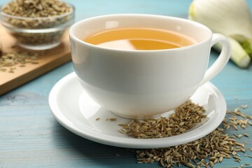 Fennel tea in cup, seeds and fresh vegetable on light blue wooden table, closeup