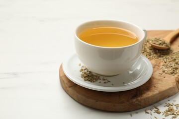 Fennel tea in cup and seeds on white marble table, closeup. Space for text