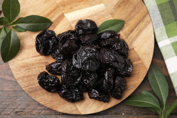 Tasty dried prunes and green leaves on wooden table, top view