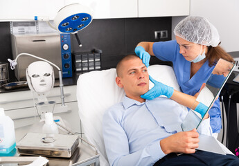 Skilled woman beautician consulting male client before facial treatment in medical esthetic office