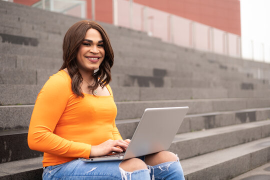 Close-up portrait of trans latin woman using laptop in campus stairs. Trans inclusion concept.
