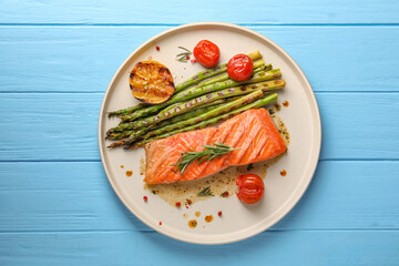 Tasty grilled salmon with tomatoes, asparagus and spices on light blue wooden table, top view