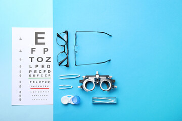 Flat lay composition with vision test chart and glasses on light blue background, space for text