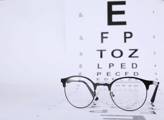Vision test chart and glasses on white background, closeup. Space for text
