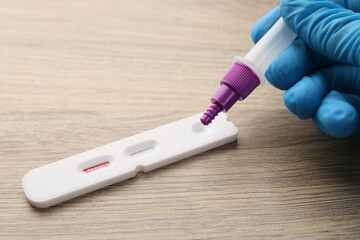 Doctor dropping buffer solution onto Covid-19 express test cassette at wooden table, closeup