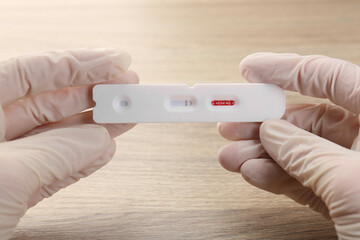 Doctor holding disposable Covid-19 express test at wooden table, closeup