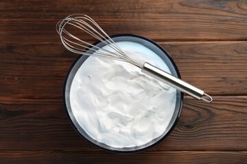 Bowl with whipped cream and whisk on wooden table, top view