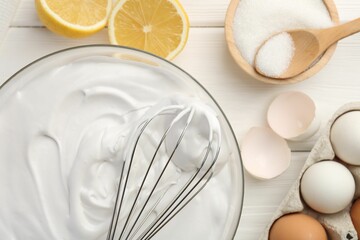 Bowl with whipped cream, whisk and ingredients on white wooden table, flat lay