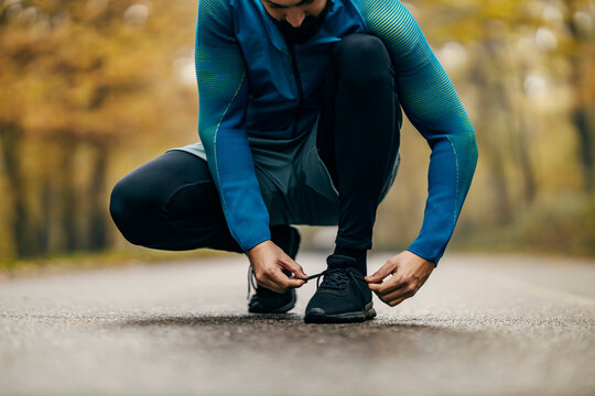 Cropped picture of a sportsman tying shoelace on roadway in nature.