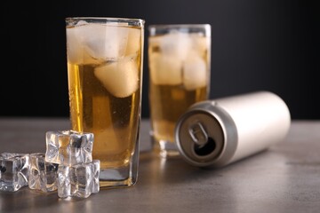Energy drink in glasses, aluminium can and ice cubes on grey table, closeup