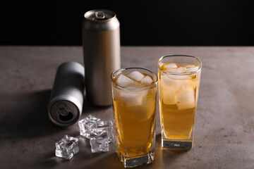 Energy drink in glasses, aluminium cans and ice cubes on grey table