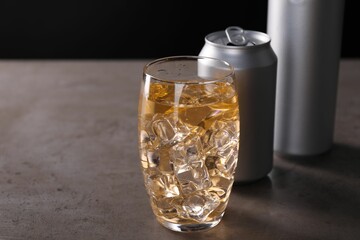 Energy drink with ice cubes in glass and aluminium cans on grey table, closeup