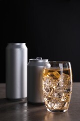 Energy drink with ice cubes in glass and aluminium cans on grey table