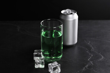 Energy drink in glass, aluminium can and ice cubes on black table