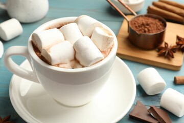 Fototapeta na wymiar Tasty hot chocolate with marshmallows and ingredients on light blue wooden table, closeup