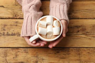 Woman with cup of tasty hot chocolate and marshmallows at wooden table, top view