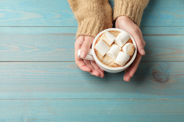 Woman with cup of tasty hot chocolate and marshmallows at light blue wooden table, top view. Space...
