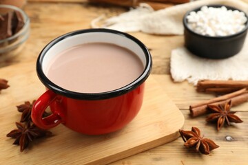 Tasty hot chocolate in cup and spices on wooden table, closeup