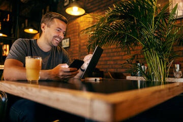 A happy man is sitting at coffee shop and using tablet and smart phone.