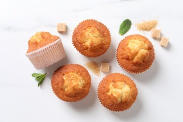 Delicious sweet muffins and brown sugar on white marble table, flat lay