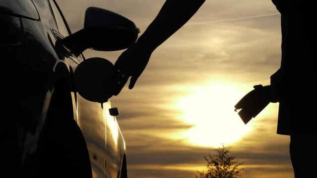 Male hand disconnects type 1 power connector from EV car, sunset in the background. Unrecognizable man unplugging charging cable, electric vehicle and charges batteries. Energy electric vehicle