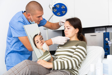 Fototapeta premium Male beautician in gloves examining face skin of young woman before procedure at cosmetology clinic