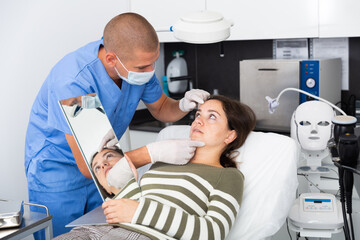 Fototapeta premium Young woman patient having consultation in aesthetic clinic, talking with confident man doctor