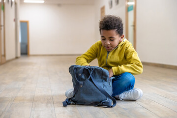 Back to school. Schoolboy with backpacks sitting on floor in school corridor during recess.