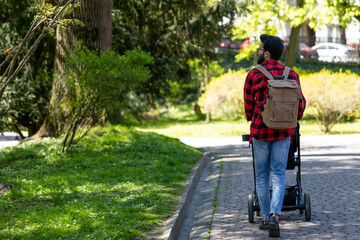 Young man in plaid shirt carrying baby carriage in the park